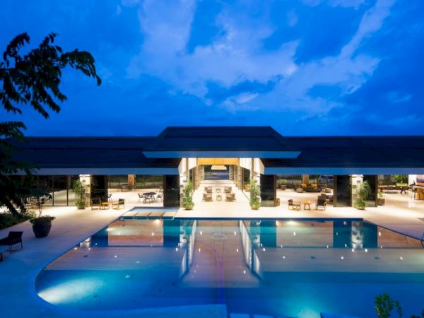 A luxurious building with a large, illuminated swimming pool and seating area, set against a twilight sky.