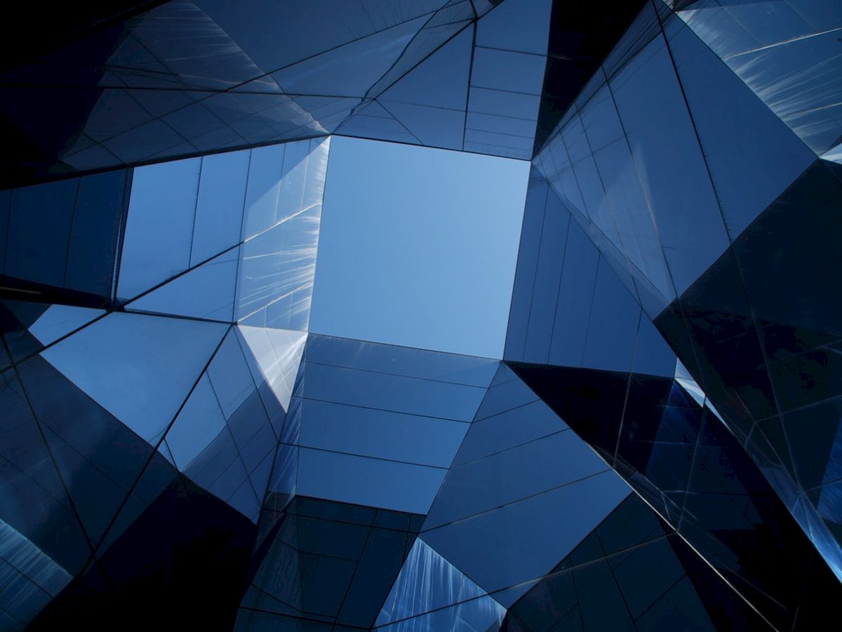 The image shows an abstract view of a glass building with geometric shapes reflecting the blue sky.