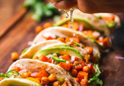 A hand squeezes lime over tacos filled with chickpeas, avocado, and vegetables on a wooden board.