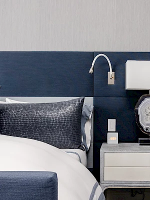 A modern bedroom with a blue headboard, white bed, a nightstand with a lamp, and elegant decor.