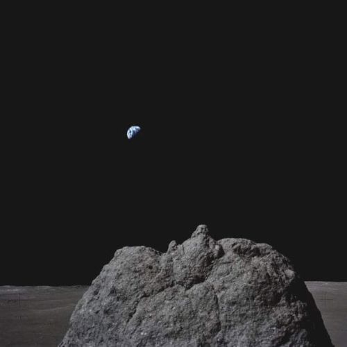 A rocky lunar surface with Earth visible in the distant black sky, showcasing a stark contrast between the Moon and Earth's appearance.