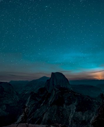 A starry night sky over a mountain landscape with a glowing horizon, creating a serene and picturesque view in the foreground.