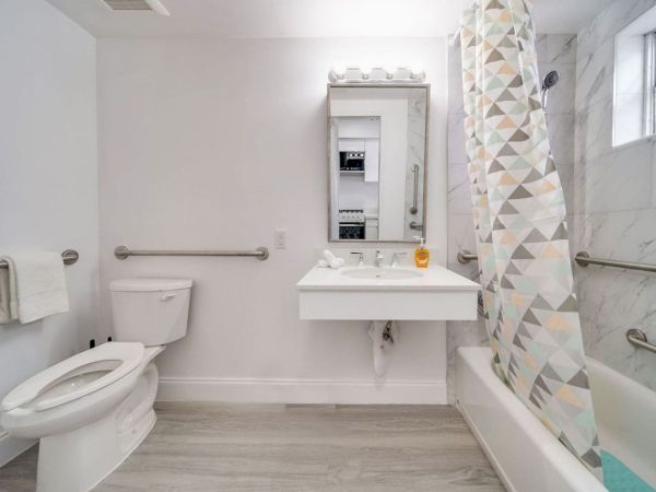 A clean, modern bathroom with a toilet, sink, mirror, bathtub, and geometric shower curtain.