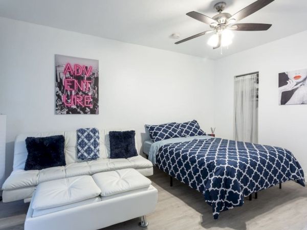 A modern bedroom with a bed, sofa, abstract art, ceiling fan, and patterned decor in blue and white tones.