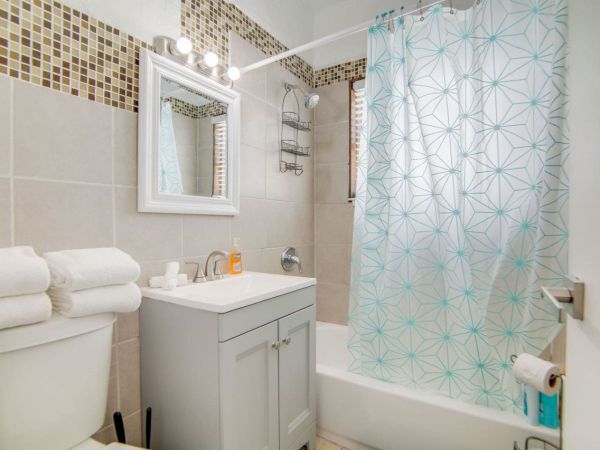A small bathroom with a vanity, towels, shower curtain with blue patterns, and a toilet beside it.