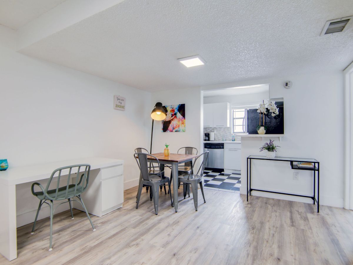 A modern dining area with a table and chairs, adjacent to a kitchen with checkered flooring and minimalist decor.