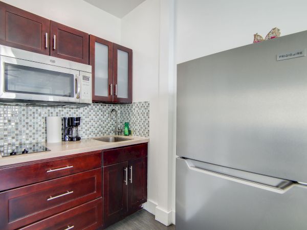 A modern kitchen corner with dark cabinets, a microwave, a coffee maker, and a stainless steel refrigerator is shown.