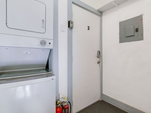 A washing machine, fire extinguisher, and a door marked "2" with an electrical panel nearby are in a small enclosed space.