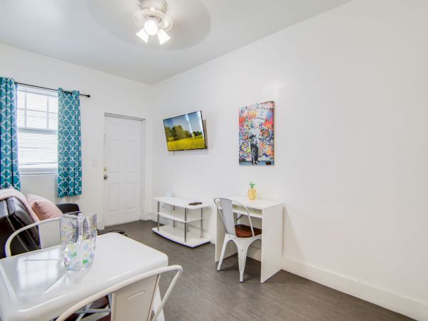 A tidy room with a table, chairs, wall-mounted TV, decorative art, and blue curtains on a window, creating a cozy atmosphere.