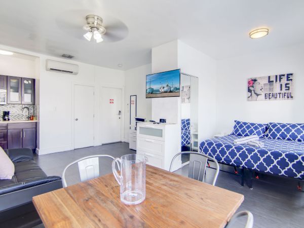 A modern studio apartment with a dining table, bed, kitchenette, and wall art saying "Life is Beautiful."