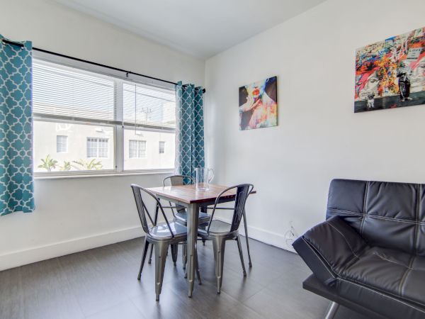 A bright room with a table, chairs, couch, blue curtains, and colorful wall art.