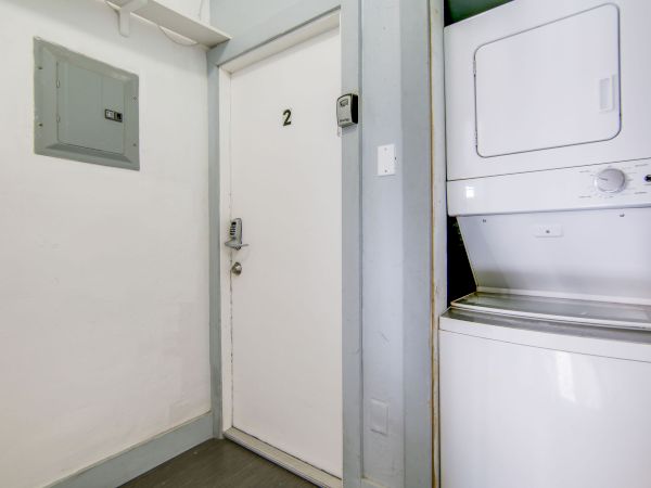A white door labeled "2" beside a stacked washer and dryer in a small laundry area. An electrical panel is visible on the wall.