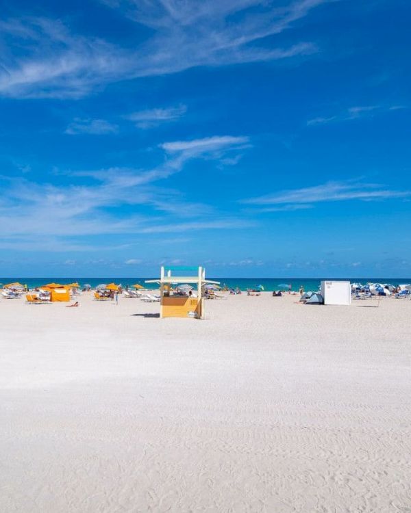 A sunny beach scene with yellow lifeguard stands, beach chairs, and umbrellas under a clear blue sky.