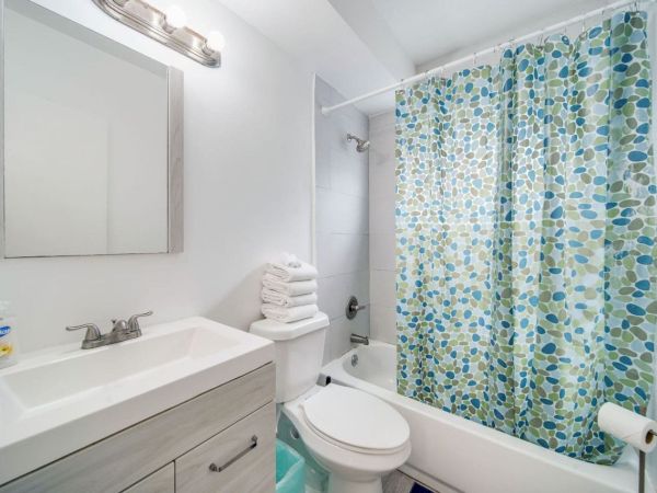 A clean, modern bathroom with a vanity, toilet, and bathtub. A shower curtain with a blue-green pattern adds color to the space.