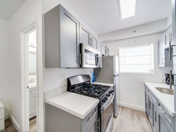 A modern kitchen features gray cabinets, a stainless steel fridge, a stove, a microwave, and a sink with a window above.