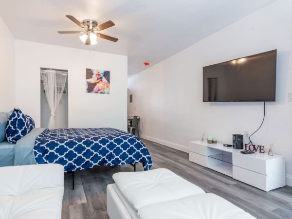 The image shows a modern bedroom with a bed, TV, ceiling fan, and white furniture, decorated in blue and white tones.