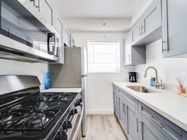 A modern kitchen with gray cabinets, a gas stove, stainless steel appliances, a sink, and window. Bright and stylish design.