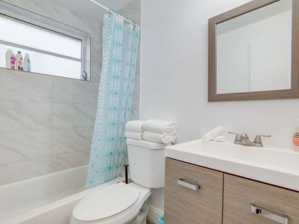 A modern bathroom with a bathtub, blue shower curtain, mirror, sink, and toilet with folded towels on top.
