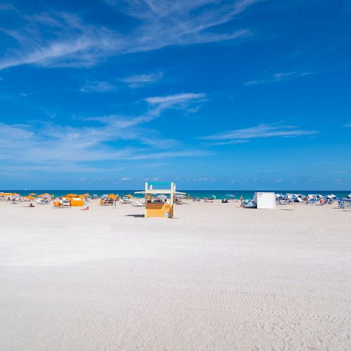 A sunny beach with white sand, scattered beach chairs, clear blue sky, and ocean waves in the background complete the serene landscape.