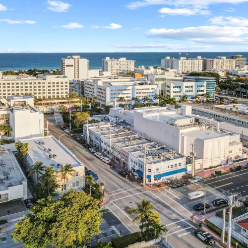 A coastal cityscape with buildings, roads, and nearby beach under a blue sky.
