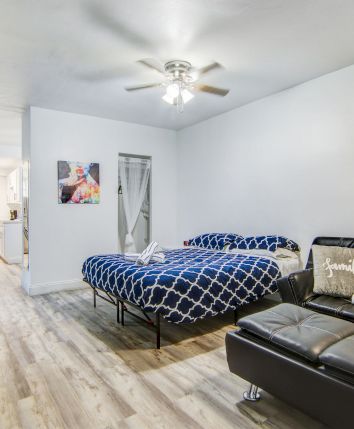 A cozy studio with a bed, sofa, and wall art stating "Life is Beautiful." There's a dining table in the background.