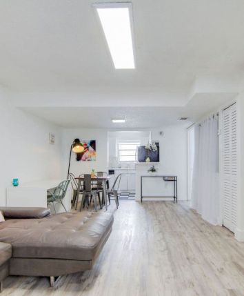 A modern living room with a sectional sofa, artworks on the wall, a dining table, and a mounted TV screen showing a landscape.