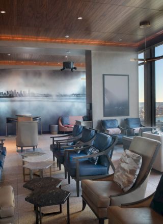 The image shows a modern lounge with sleek chairs, a panoramic mural, and large windows offering a scenic view of water and landscape.