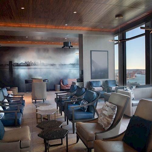 A modern lounge with seating, large windows, and a cityscape mural on the wall.