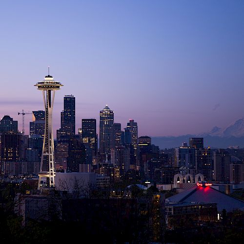 A city skyline at dusk with a distinctive tower and a mountain in the background.