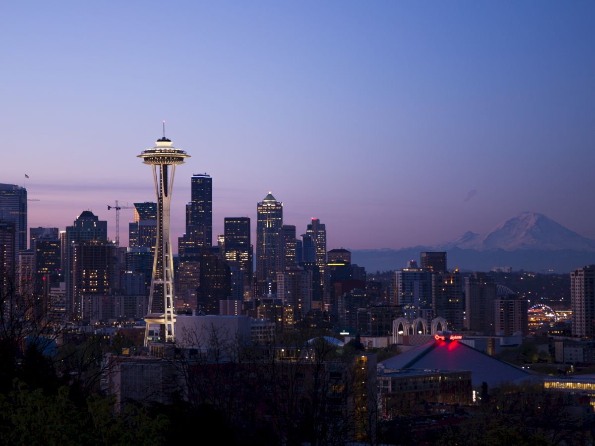 A nighttime city skyline featuring a prominent tower and distant mountain, under a dusky twilight sky.