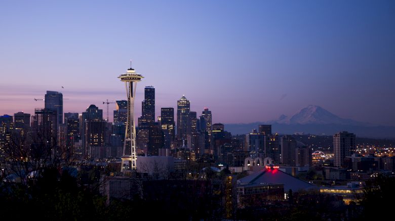 A nighttime city skyline featuring a prominent tower and distant mountain, under a dusky twilight sky.